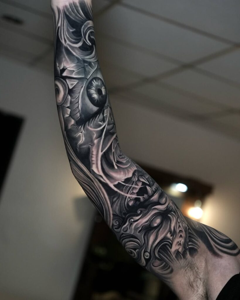 A detailed black and grey sleeve tattoo with eye and swirl patterns on an arm.