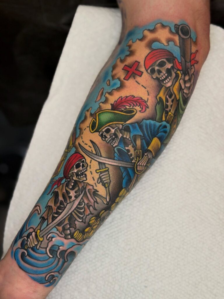 An American traditional pirate tattoo on a forearm featuring three skeletons with weapons and pirate hats.