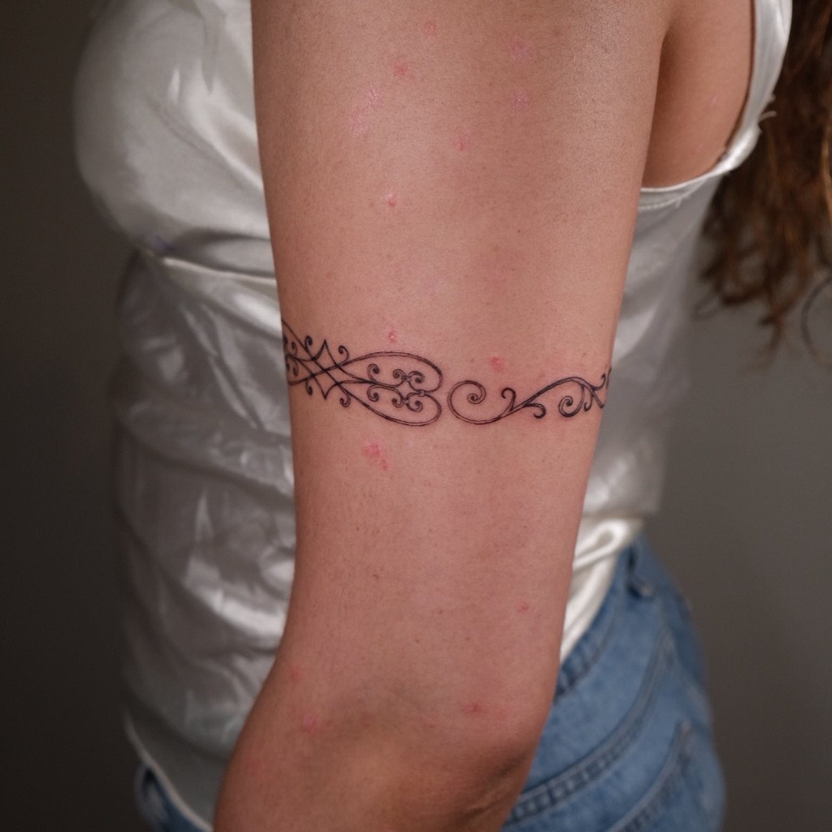 A black scrollwork tattoo wraps around a person's upper arm like a decorative cuff.