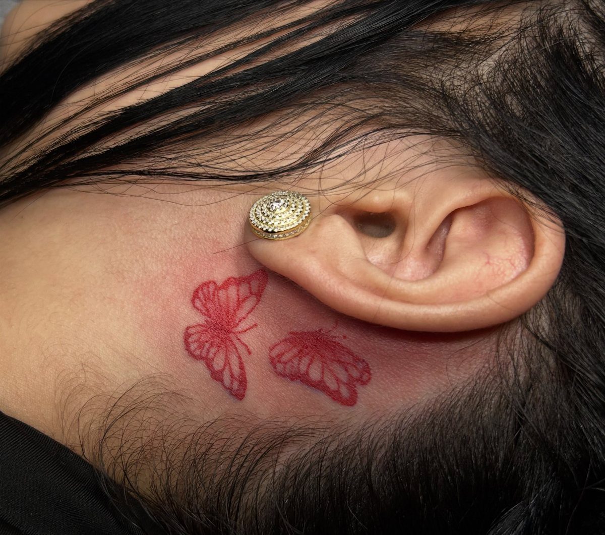 Two small red butterfly tattoos located on the skin behind a person's ear.