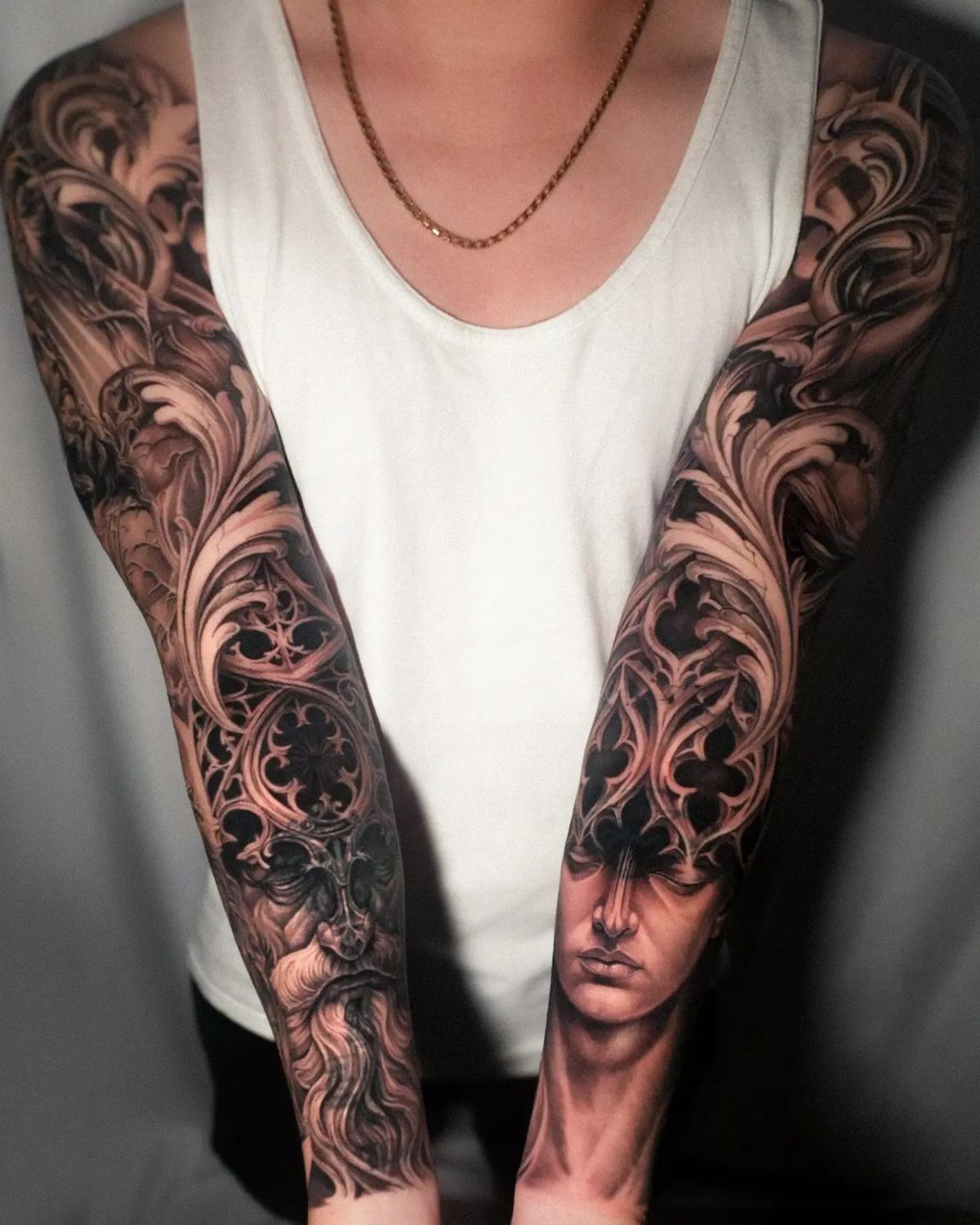 Person displaying detailed black and grey filigree sleeve tattoos on both arms.