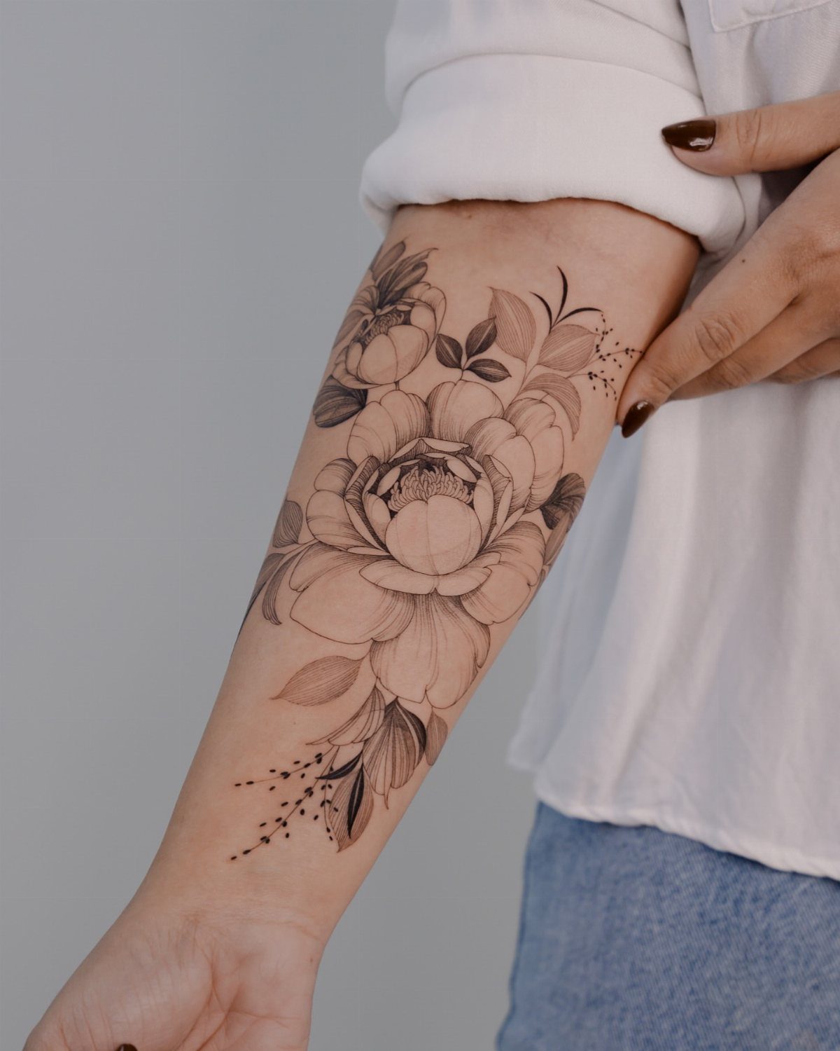 A detailed fine line floral tattoo of a peony on a person's forearm.