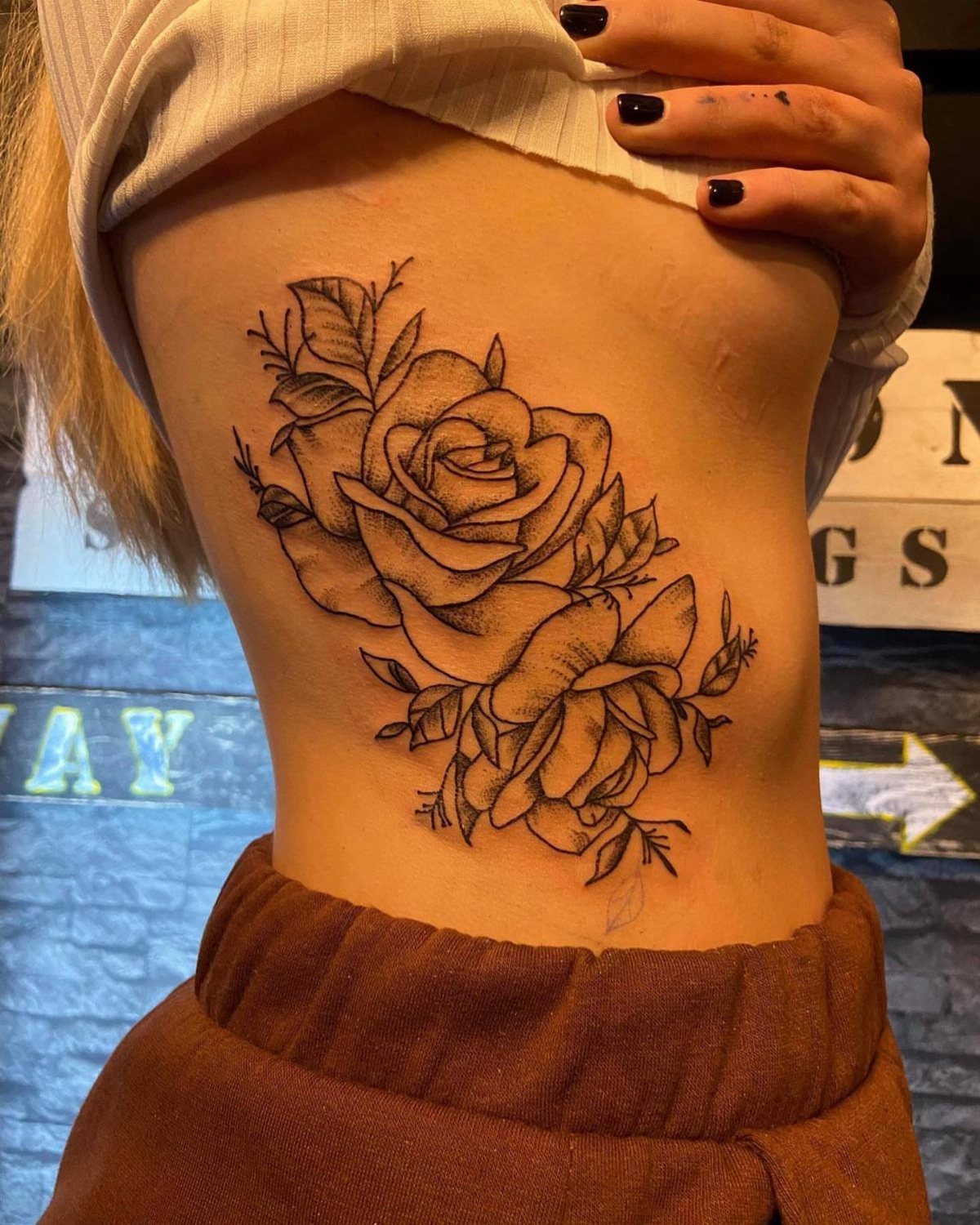 Black ink rose tattoo on a person's ribcage side profile.