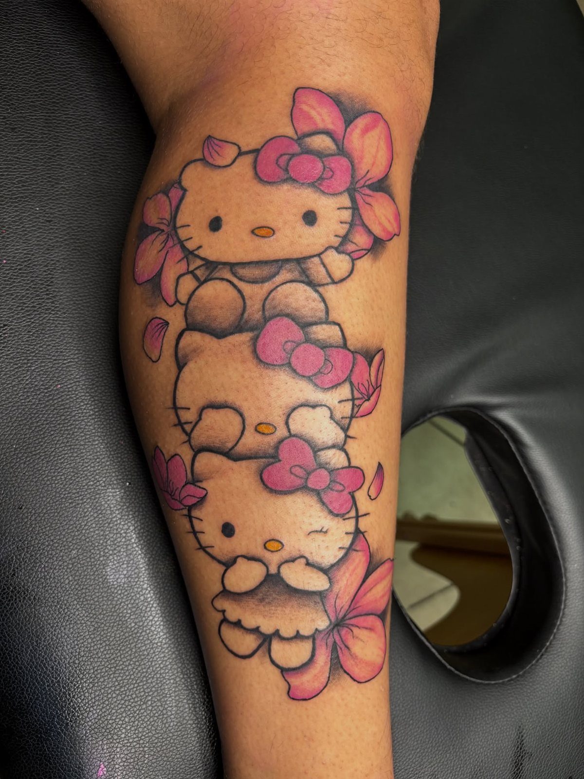 Two Hello Kitty characters tattooed vertically on a person's forearm with pink bows and flowers.