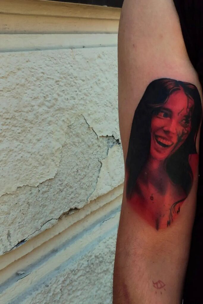 A large red and black monochromatic portrait tattoo of a smiling woman on an arm.