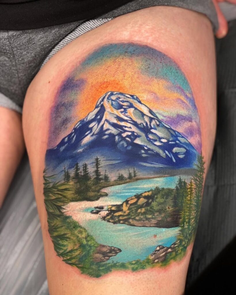 A colorful mountain landscape tattoo on skin featuring a snowy peak, river, and pine trees.