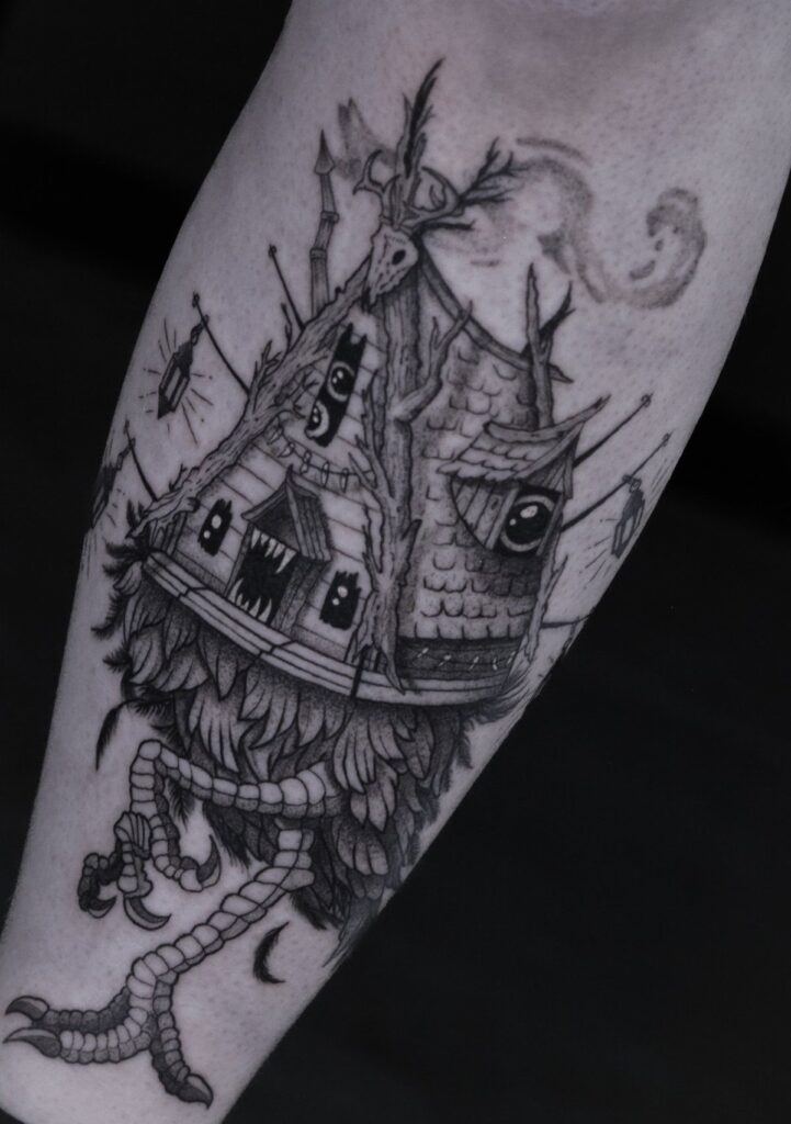 A black and grey tattoo of a mythical wooden hut with eyes and bird legs.