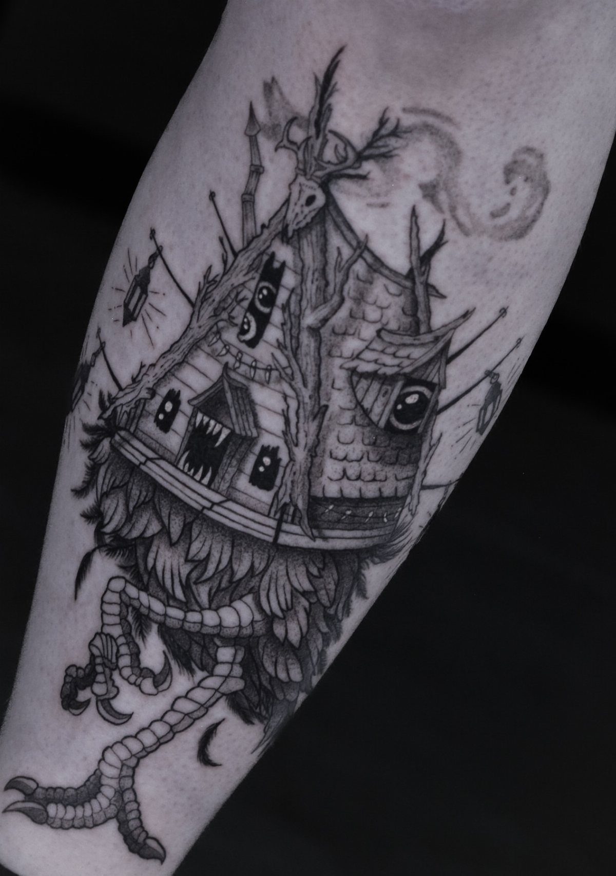 A black and grey tattoo of a mythical wooden hut with eyes and bird legs.