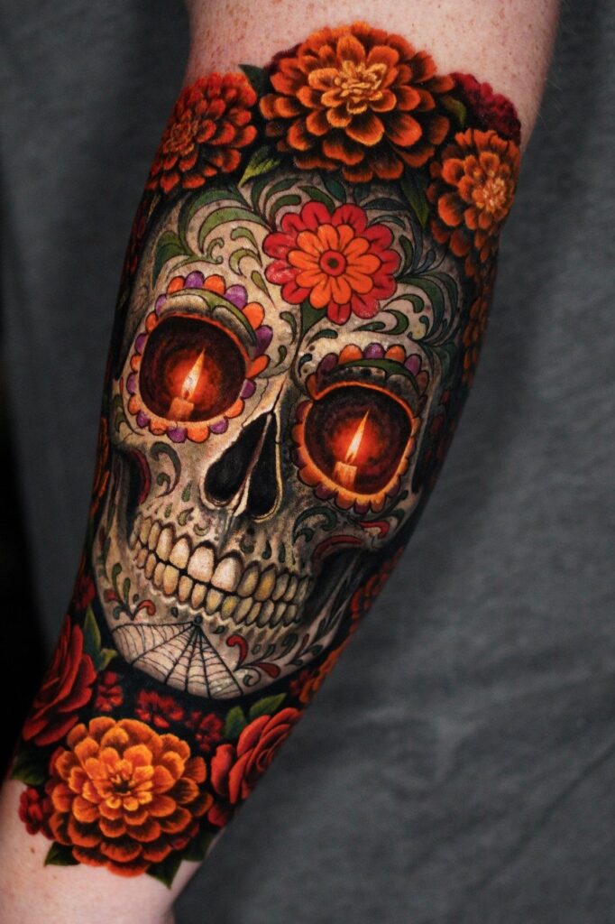 A colorful sugar skull tattoo with candle eyes and orange marigold flowers on a forearm.