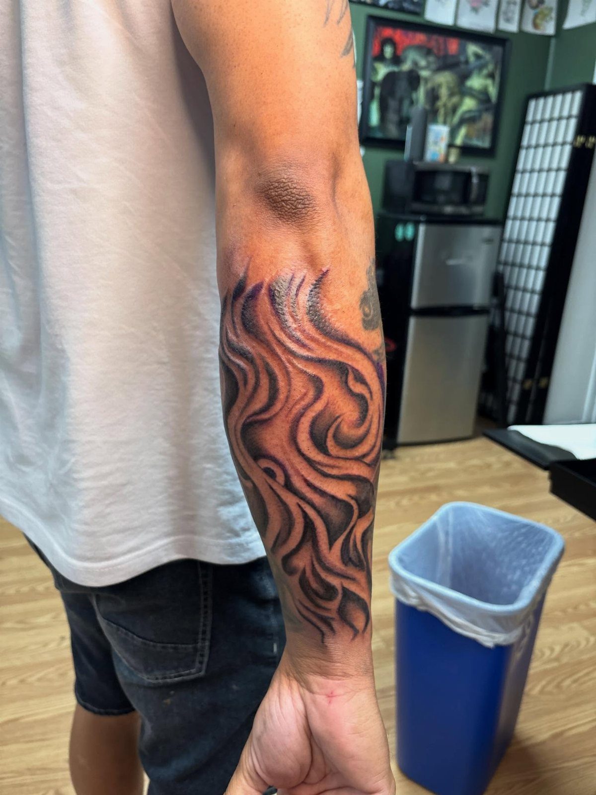A man's forearm displaying a large black ink tattoo of swirling smoke patterns.