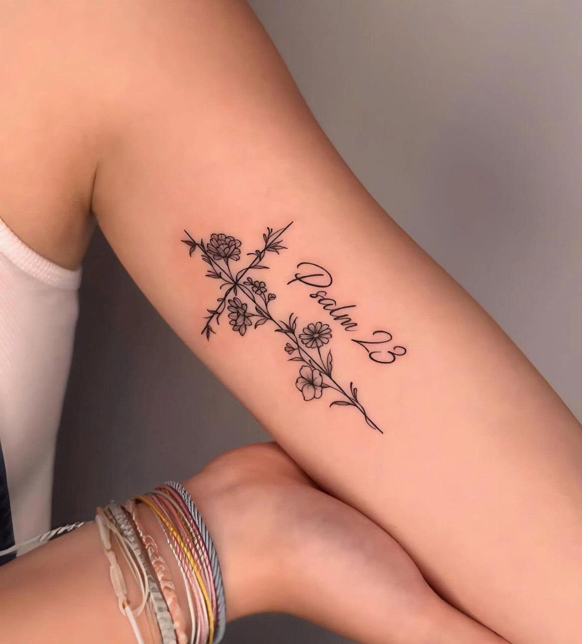 A black ink tattoo of a floral cross and the text Psalm 23 on an arm.