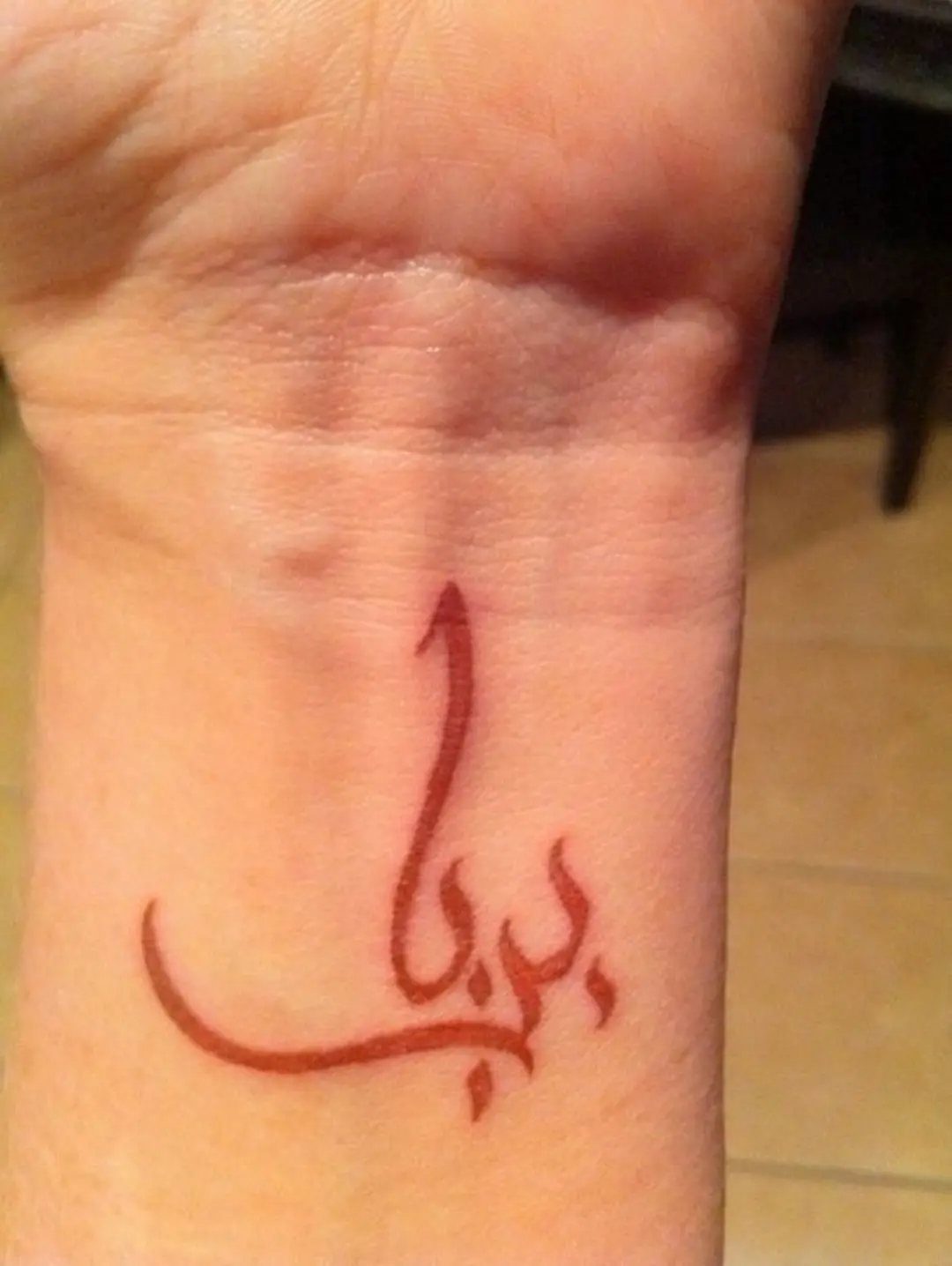 A red ink Arabic calligraphy tattoo on a person's inner wrist.