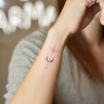 A minimalist crescent moon and star tattoo on the side of a person's wrist.