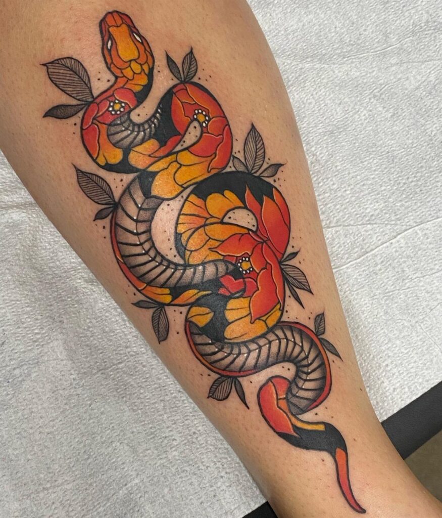 A colorful traditional snake tattoo with orange flowers and leaves on a person's leg.