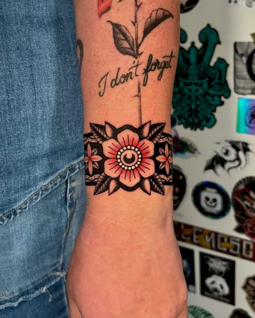 A person's forearm displaying a traditional red and black floral band tattoo around the wrist.