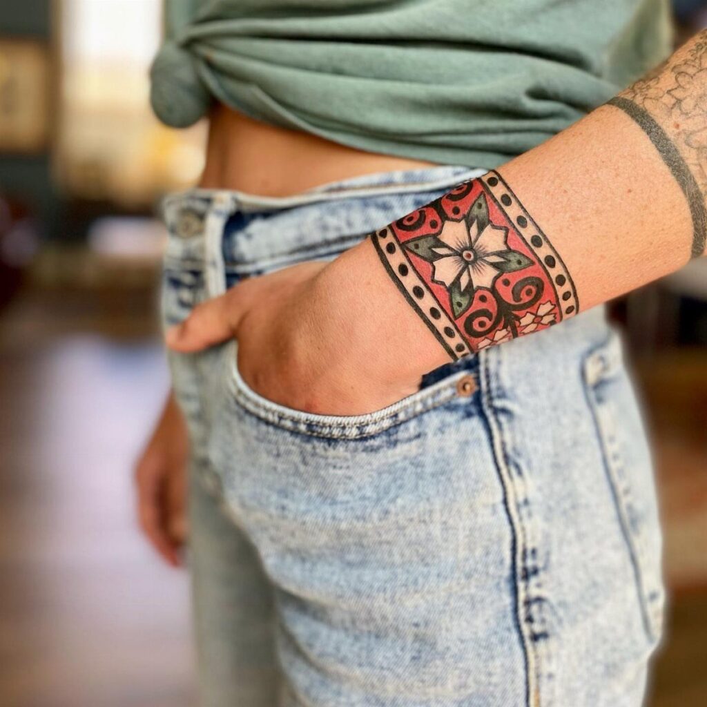 A person's forearm displaying a colorful traditional floral tattoo cuff design.