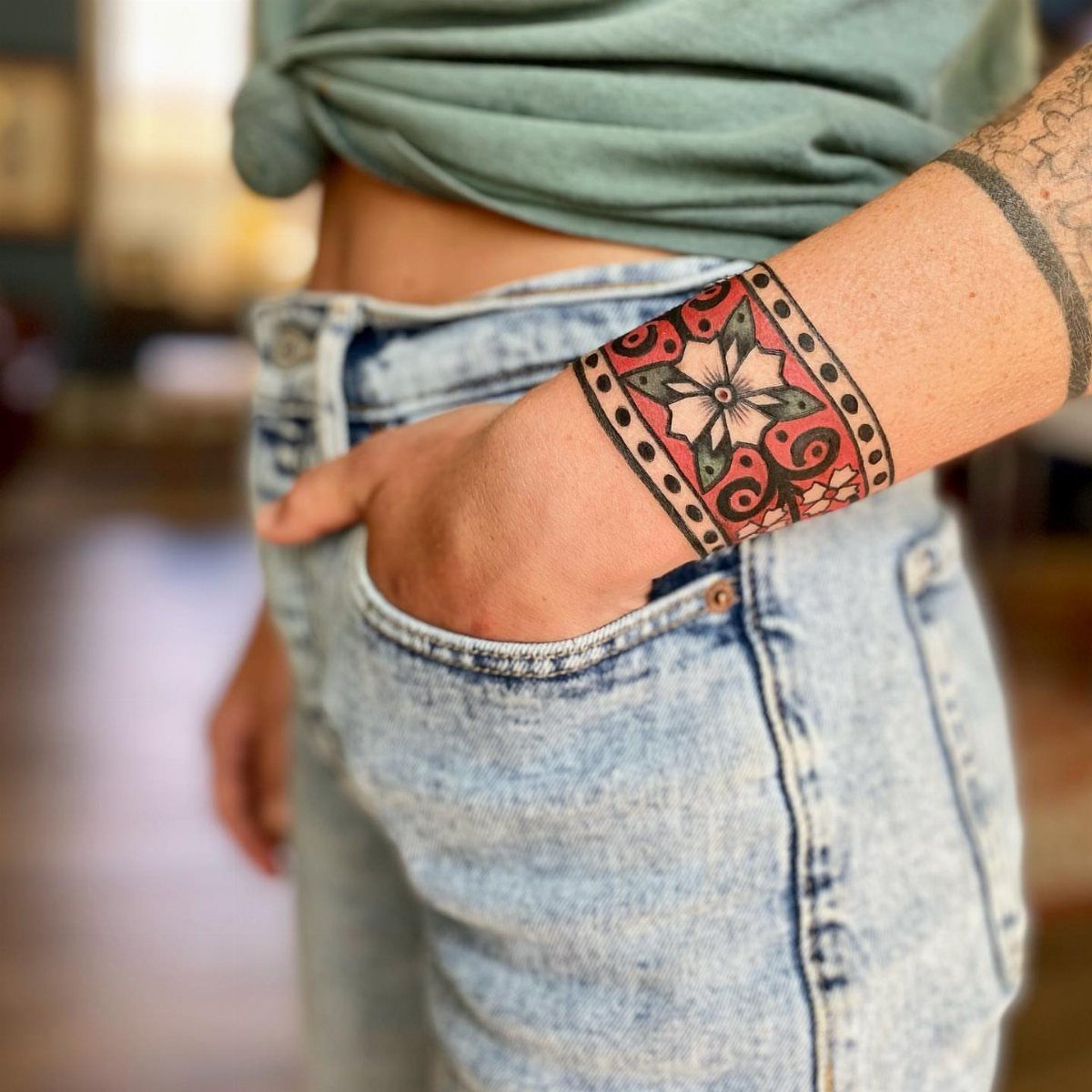 A person's forearm displaying a colorful traditional floral tattoo cuff design.